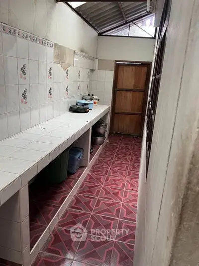 Narrow kitchen area with tiled countertops and red patterned floor tiles, featuring a closed layout.