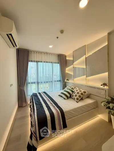Modern bedroom with stylish decor and large window offering city views, featuring elegant lighting and cozy bedding.