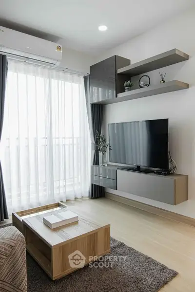 Modern living room with sleek furniture and large TV, featuring natural light from floor-to-ceiling windows.