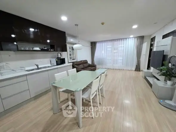 Modern open-layout living room with sleek kitchen, dining area, and large window for natural light.