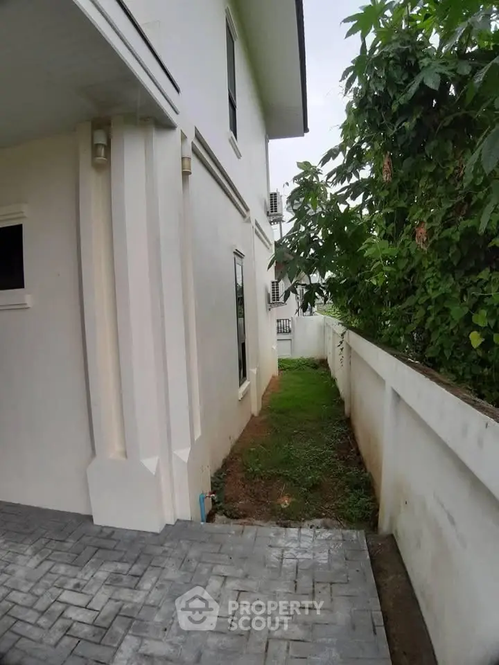 Charming side view of a modern house with lush greenery and paved walkway.