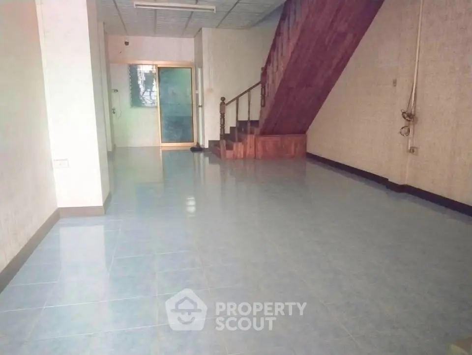 Spacious empty room with tiled floor and wooden staircase, ideal for customization.