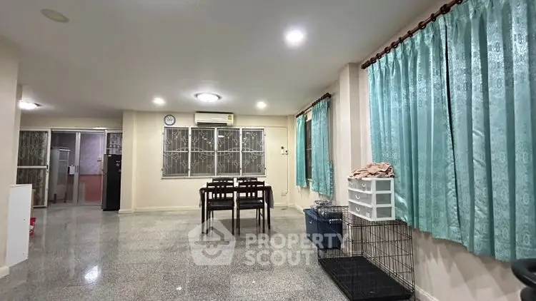 Spacious living room with dining area and large windows, featuring elegant curtains and modern lighting.
