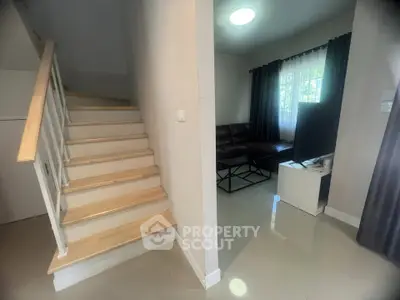 Modern living room with staircase and natural light, featuring sleek furniture and stylish decor.