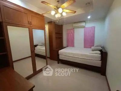 Cozy bedroom with wooden furniture and ceiling fan, featuring a mirrored wardrobe and air conditioning.