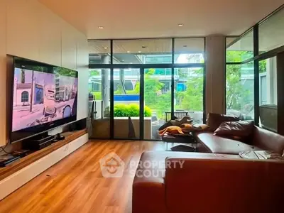 Spacious living room with modern decor and large TV, featuring floor-to-ceiling windows and garden view.
