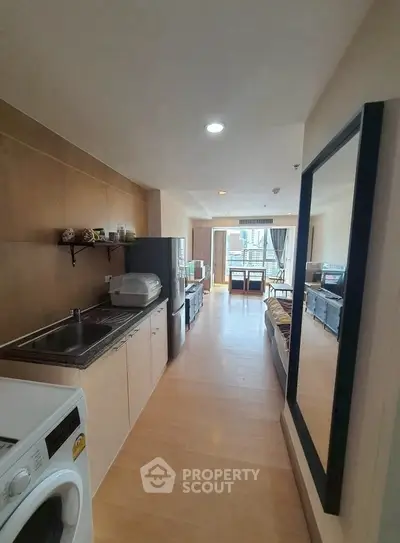 Modern studio apartment with open layout and balcony view, featuring a washing machine and sleek kitchen area.