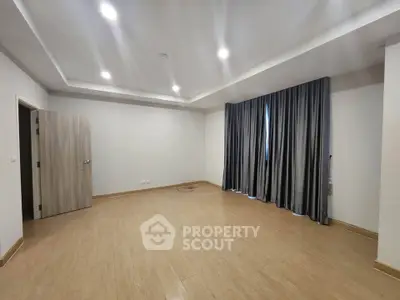 Spacious empty room with wooden flooring and elegant curtains, ideal for customization.