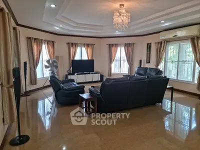 Spacious living room with elegant chandelier and leather sofas, perfect for family gatherings.