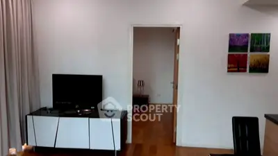 Modern living room with sleek TV stand and wooden flooring, leading to a cozy hallway.