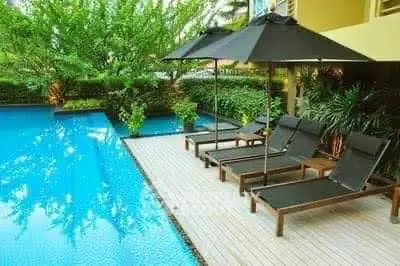 Luxurious poolside area with sun loungers and umbrellas in a serene garden setting.