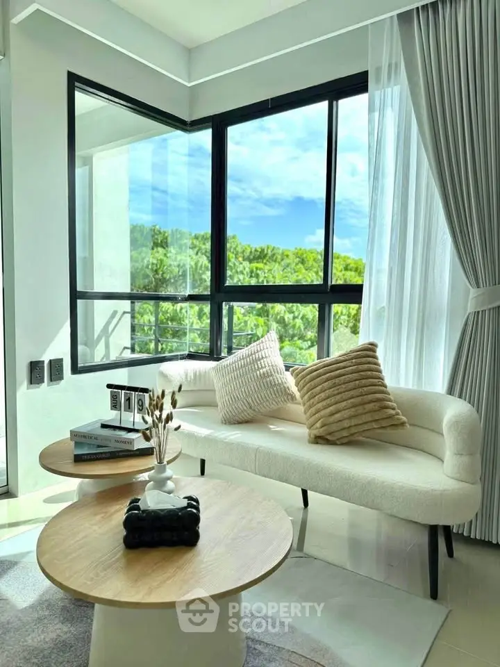 Bright living room with modern decor and large windows offering lush green views.
