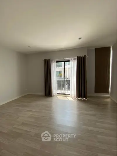 Spacious empty room with wooden flooring and large window for natural light.