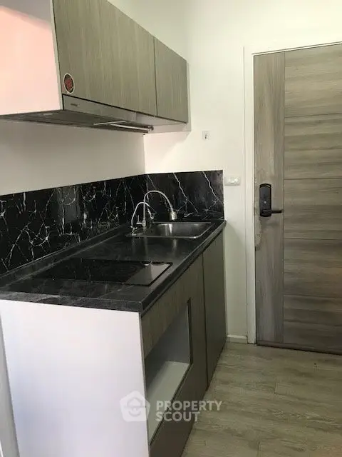 Modern compact kitchen with sleek black marble countertops and wooden cabinetry.
