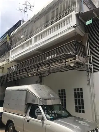 Three-story building with metal balcony and parked truck in urban setting