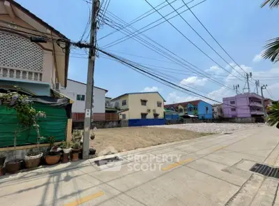 Vacant land plot in a residential neighborhood with clear blue sky, ideal for development opportunities.