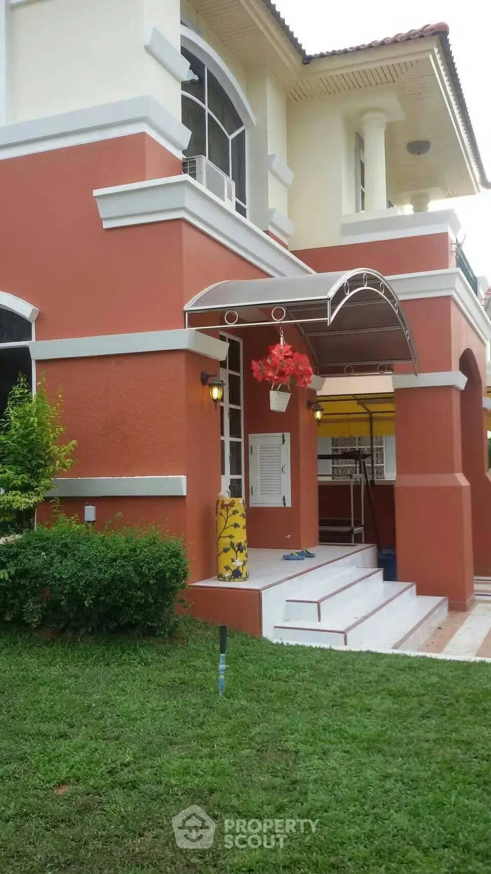 Charming two-story house with vibrant red exterior and lush green lawn, featuring a welcoming entrance.