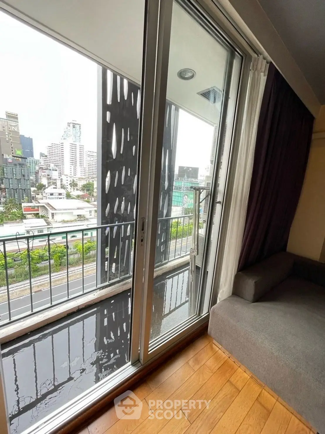Modern apartment with balcony and city view, featuring floor-to-ceiling windows and wooden flooring.