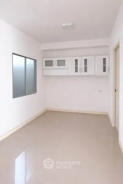 Spacious empty room with sleek white cabinets and large window, perfect for customization.