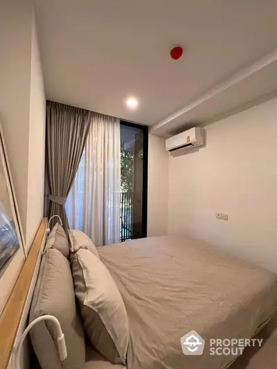 Cozy bedroom with a comfortable queen-sized bed, modern air conditioning unit, and access to a private balcony through sliding glass doors, complemented by elegant drapery.