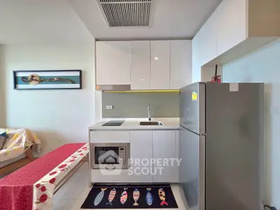 Modern compact kitchen with sleek white cabinets and stainless steel appliances in a cozy apartment.
