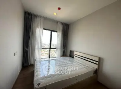 Spacious bedroom with large window offering stunning city views, featuring a modern bed and elegant curtains.