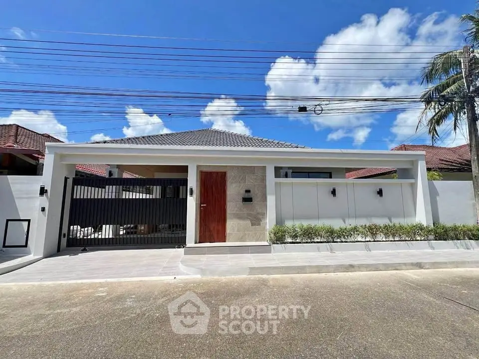 Modern single-story house with sleek design and gated entrance under a clear blue sky.