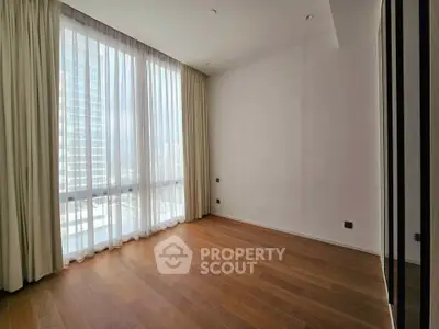 Spacious empty room with large window and wooden flooring in modern apartment.