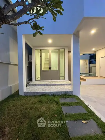 Modern home entrance with glass doors and lush garden, featuring a sleek poolside view.