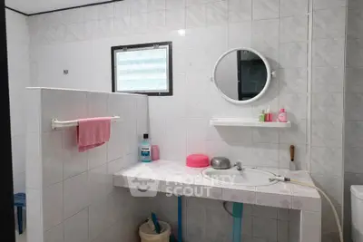 Cozy bathroom with tiled walls, round mirror, and essential toiletries for a comfortable living experience.