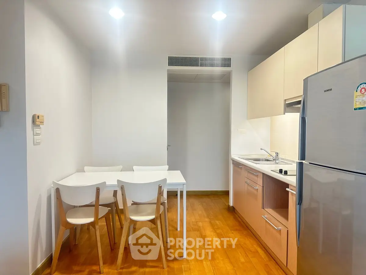 Modern kitchen with dining area, featuring sleek cabinetry and stainless steel fridge in a cozy apartment.
