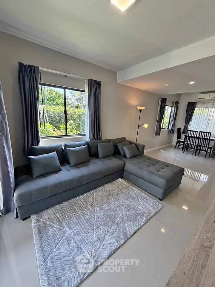 Spacious modern living room with large gray sectional sofa and dining area, featuring natural light.