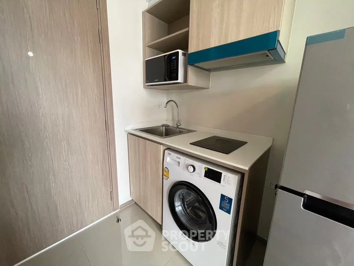 Modern compact kitchen with washing machine and microwave in sleek apartment.
