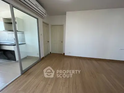 Spacious modern living room with wooden flooring and glass sliding doors leading to a sleek kitchen.