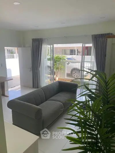 Bright living room with modern sofa and large windows overlooking garden area.