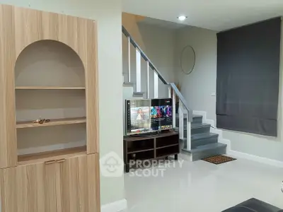 Modern living room with staircase and wooden cabinet, featuring a sleek TV setup.