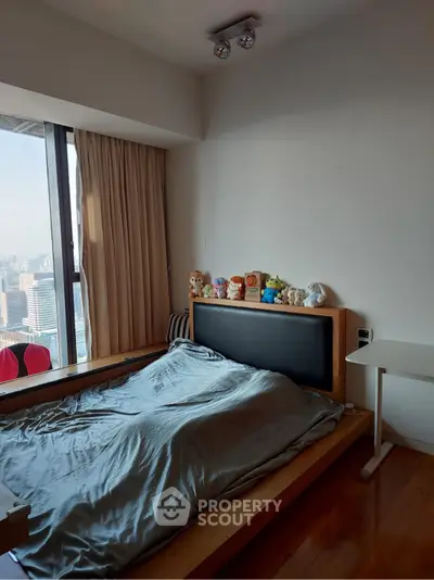 Cozy bedroom with city view, featuring a modern bed and plush toys on the headboard, perfect for urban living.