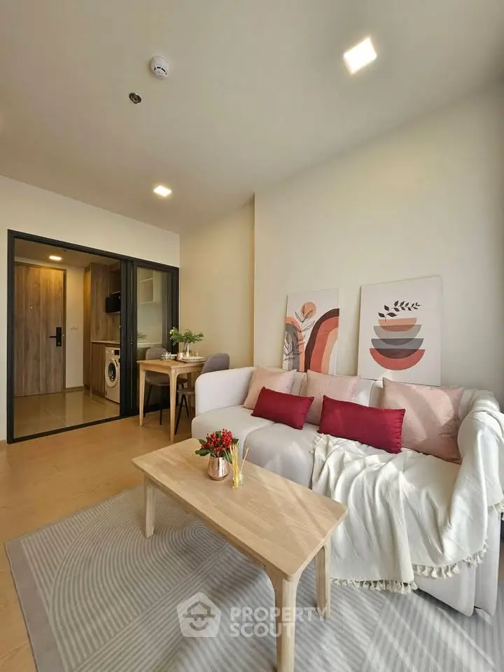 Modern living room with cozy decor and open view to dining area, featuring stylish furniture and artwork.