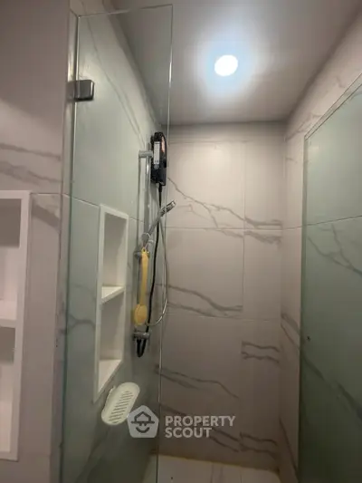 Modern bathroom with glass shower and marble tiles, featuring built-in shelves for a sleek design.