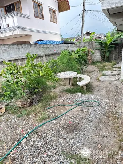 Charming garden area with stone table and bench, surrounded by greenery, perfect for outdoor relaxation.