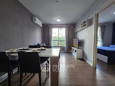 Modern living room with dining area and view into bedroom, featuring sleek furniture and natural light.