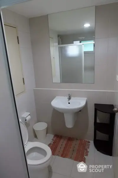 Pristine white bathroom with modern fixtures, large mirror, and neutral tiles, offering a clean and serene personal space.