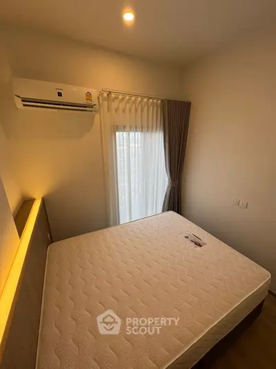 Cozy bedroom with natural light, featuring a comfortable mattress and modern air conditioning unit.