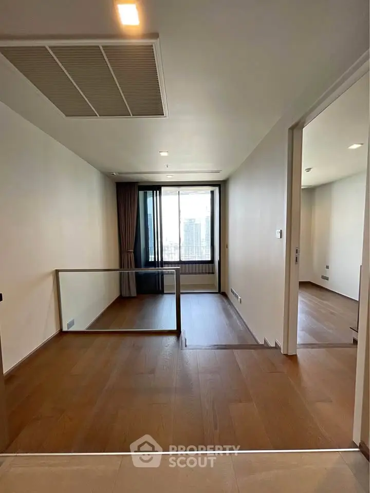 Spacious modern living area with wooden flooring and large window offering city views.