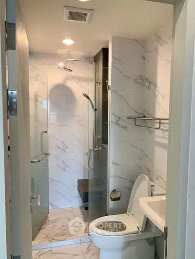Modern bathroom with glass shower and marble tiles, featuring sleek fixtures and contemporary design.
