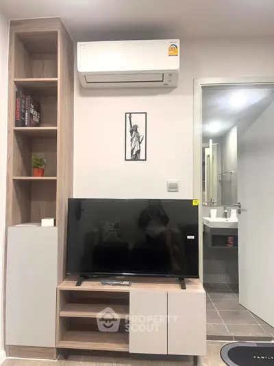 Modern living room with air conditioner and TV, featuring stylish shelving and bathroom access.