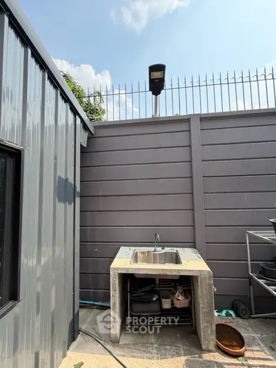 Outdoor utility sink area with metal fencing and storage space