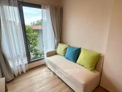 Cozy living room with a beige sofa and colorful cushions, featuring large windows with sheer curtains.