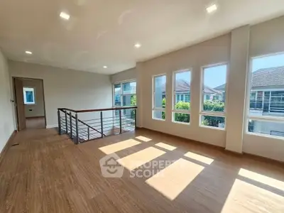 Spacious sunlit room with large windows and wooden flooring in modern home