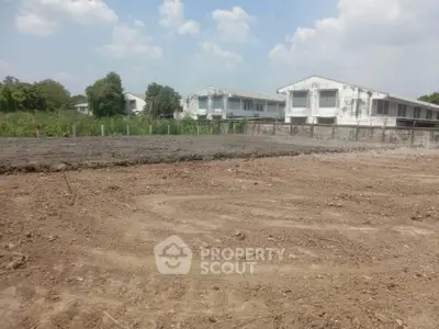 Expansive vacant land ready for development, showcasing potential with a backdrop of modern white residential structures under a clear sky.